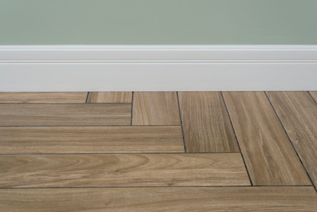 Interior concept. Light matte wall, white baseboard and tiles immitating hardwood flooring
